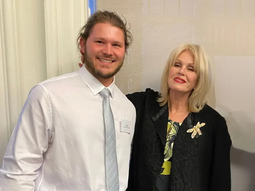 Louis Wright, in a white shirt and grey tie, standing indoors beside Joanna Lumley.